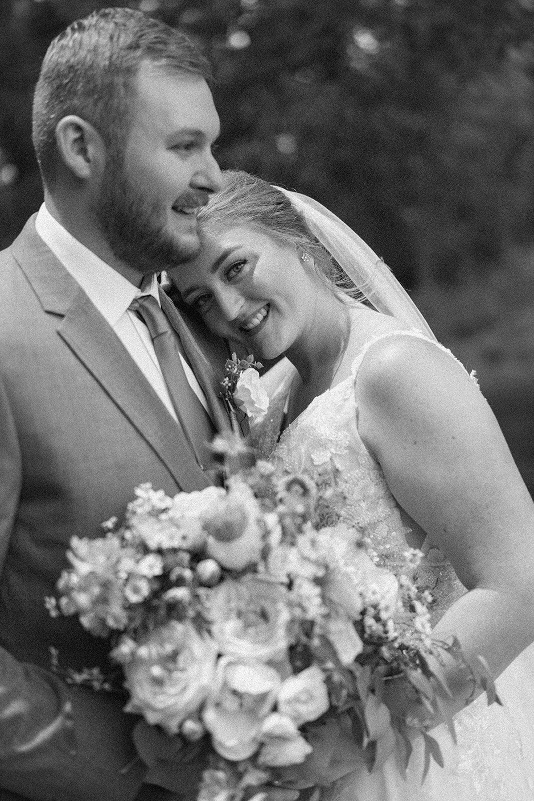 Romantic moment of the bride resting her chin on the groom’s shoulder during portraits at The Blue Heron Barn.