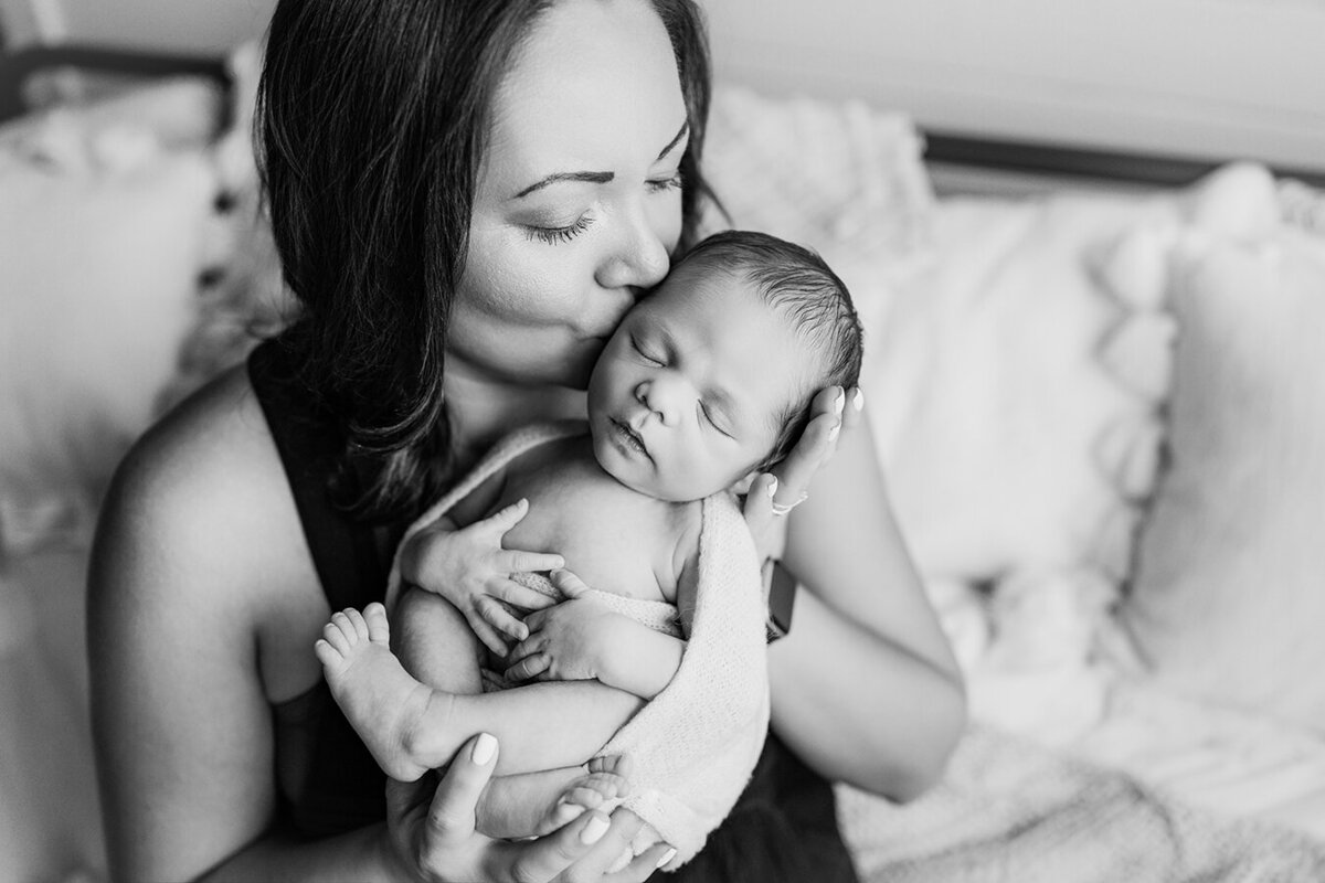 New mom kissing newborn baby boy in black and white