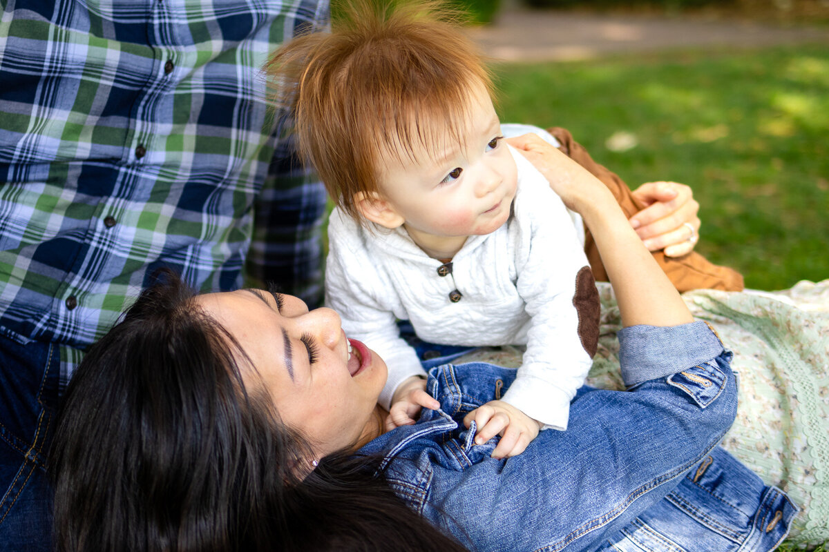 Family lying on the grass with their baby boy during a relaxed outdoor lifestyle session in San Mateo