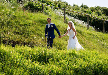 A bride and groom holding hands walking up a hill