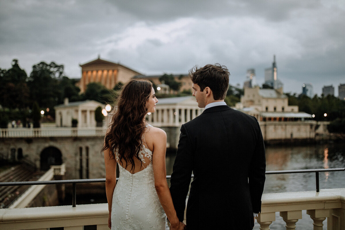 Bride and groom holding hands looking at each other while standing in front of rolling hills with the sunlight coming down on them