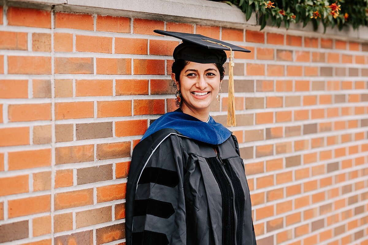 UNC Graduate in cap and gown leaning against a brick wall in North carolina