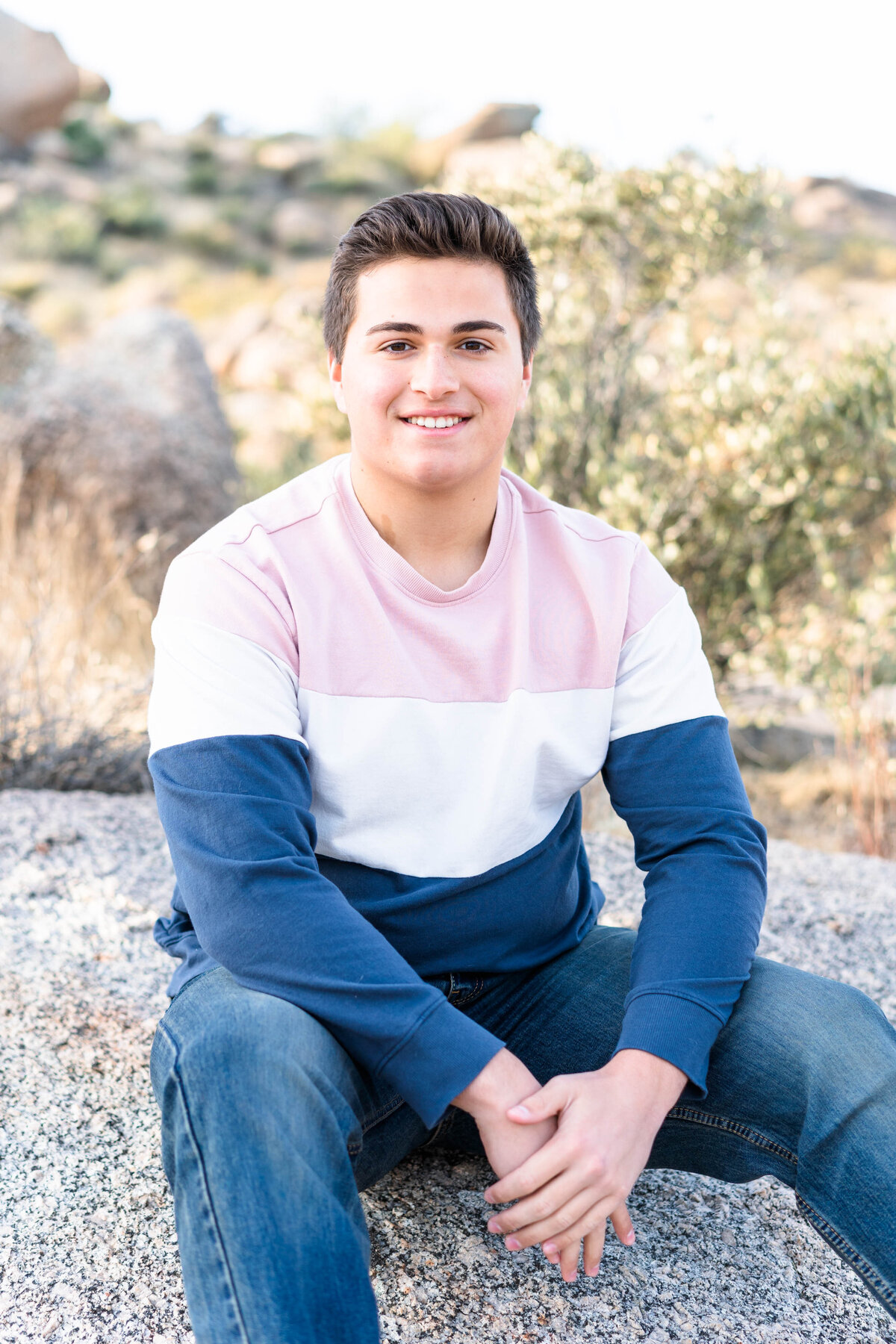 High school boy sitting on rock in desert smiling