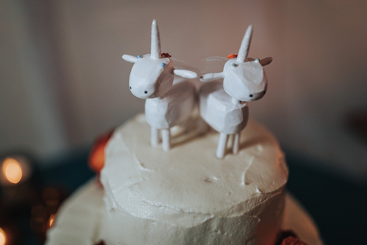 Two hand carved white wood unicorns sit on top of a white wedding cake.