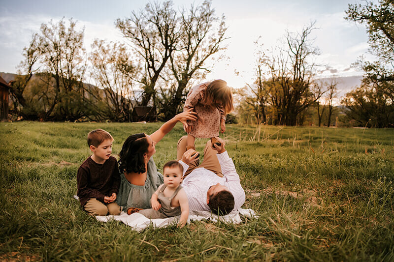 Family cuddles on the ground of a grassy field in Boulder with a brown barn in the background