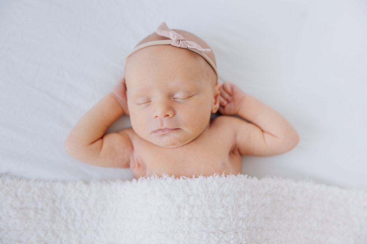 newborn girl laying on white bed with hands behind head