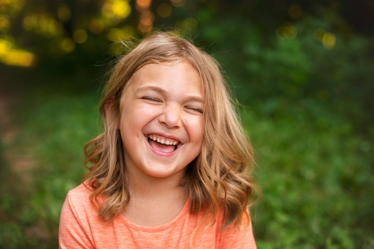 A-young-girl-laughing-in-an-orange-dress-during-an-outdoor-family-photo-session-at-Glenns-Valley-Nature-Park-in-the-Center-Grove-area-of-Greenwood-Indiana-my-favorite-park-for-family-sessions