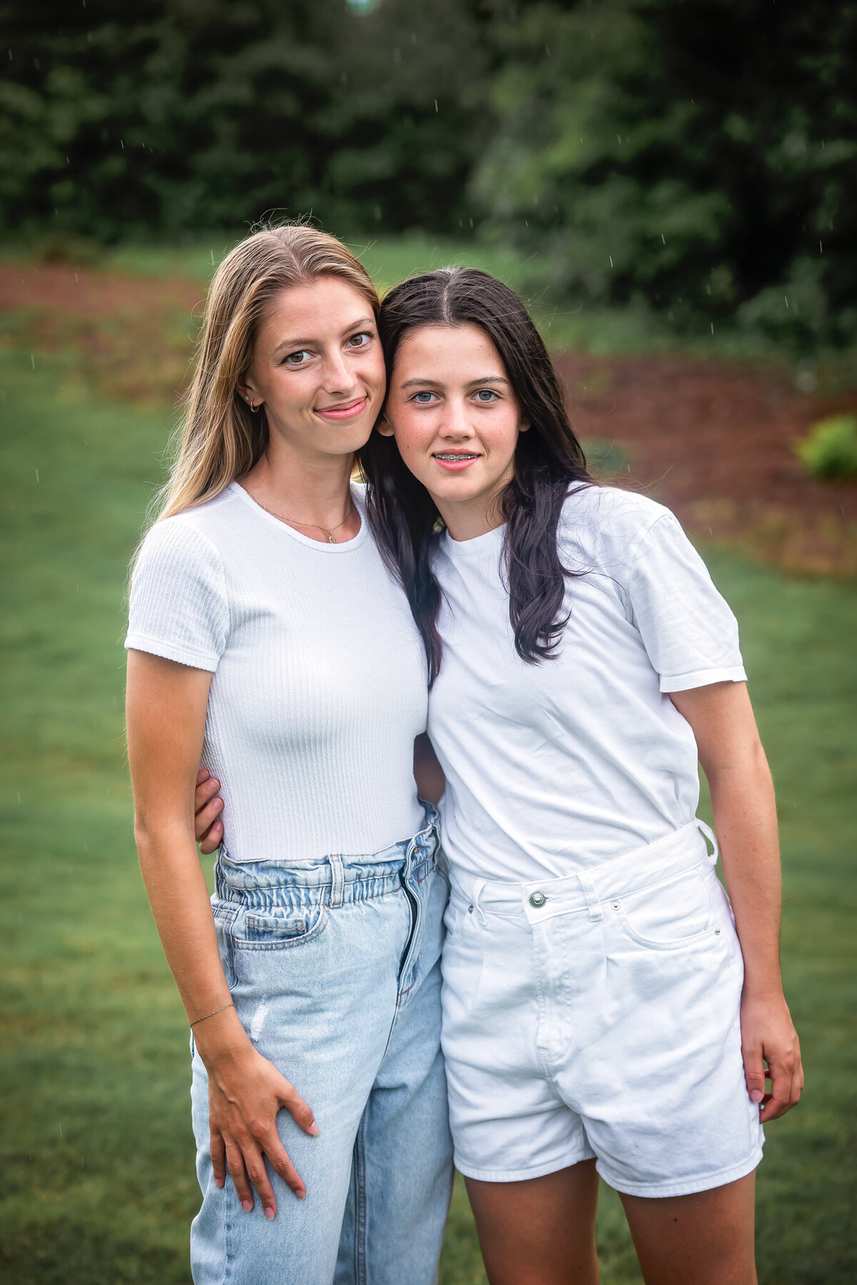 Two young sisters dressed in white shirts are standing beside each other and smiling.