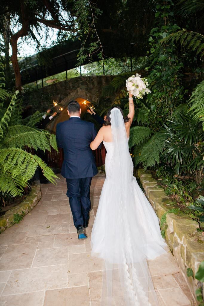 A bride and groom walking away while she holds up a bouquet