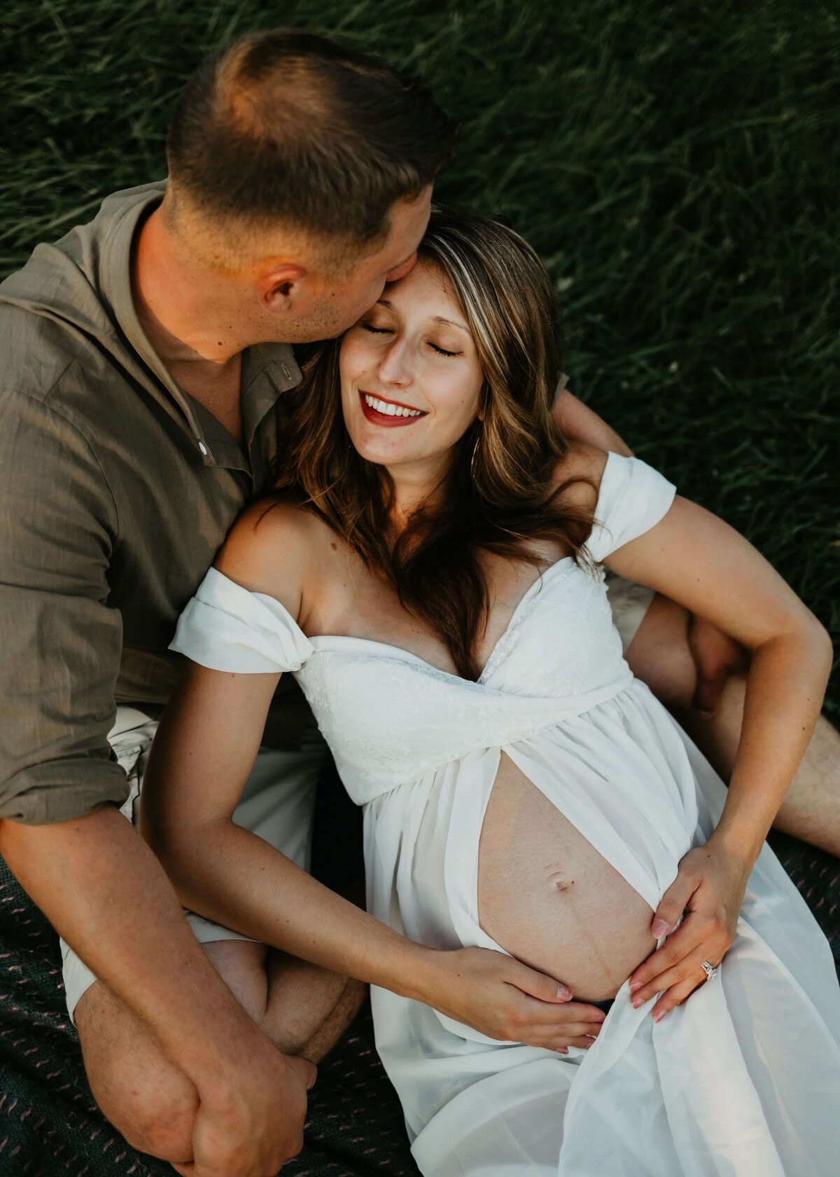 A pregnant woman and her husband are lounging on a blanket in the grass, captured by a Pittsburgh maternity photographer.