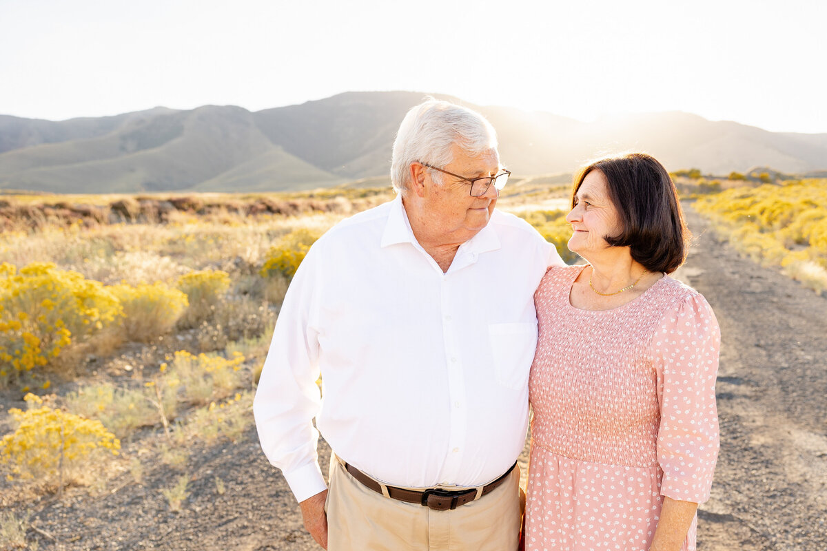 An elderly couple standing together in a golden sunset, gazing at each other with love.