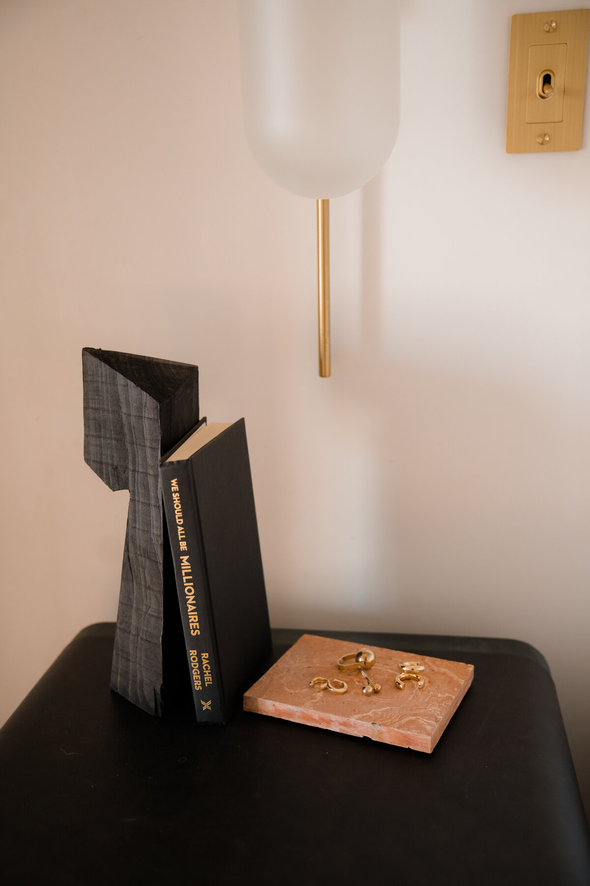 Decorative sculpture, We Should All Be Millionaires book by Rachel Rodgers, and jewelry laid out on a black table