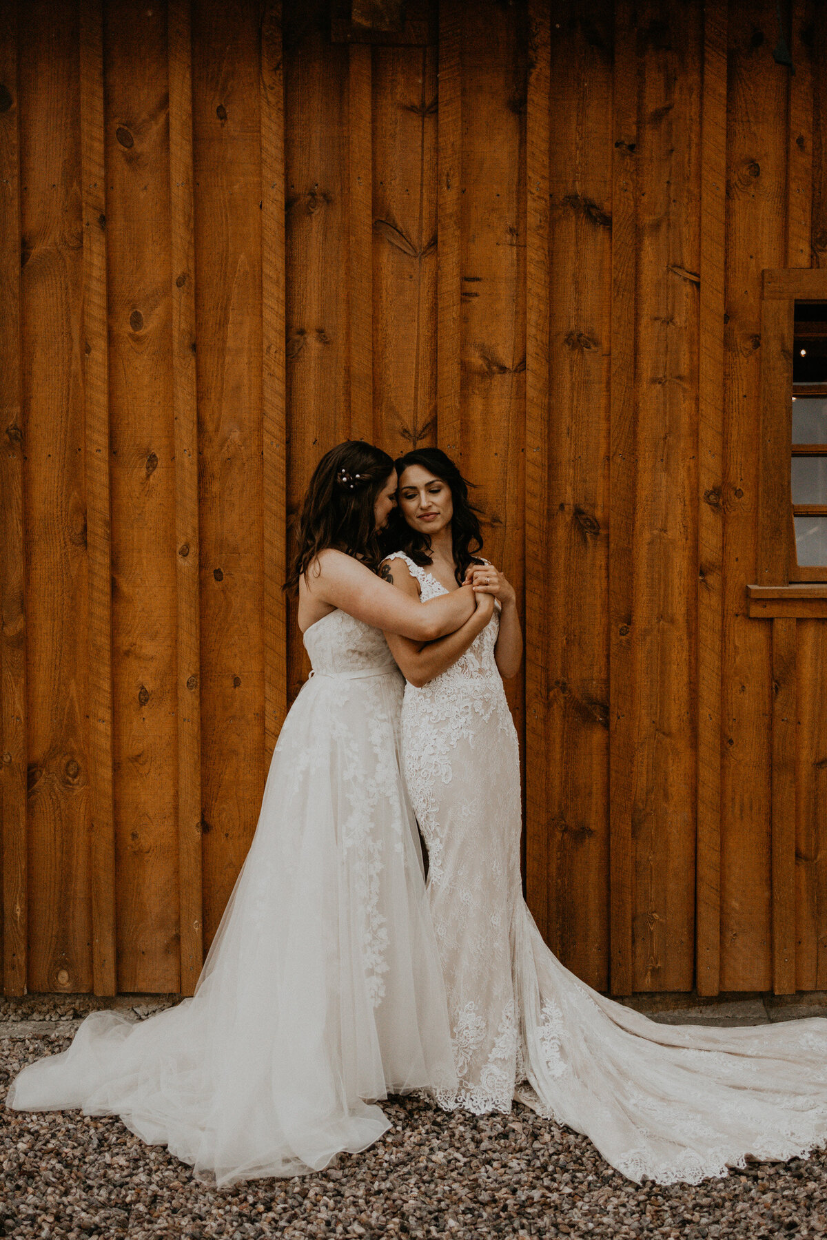 two brides standing in front of a barn in their wedding dresses