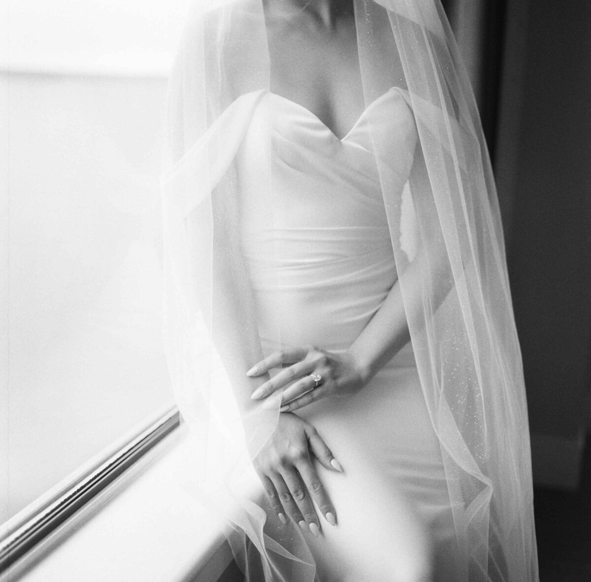 black and white square image of brides hands and ring resting gently on her lap