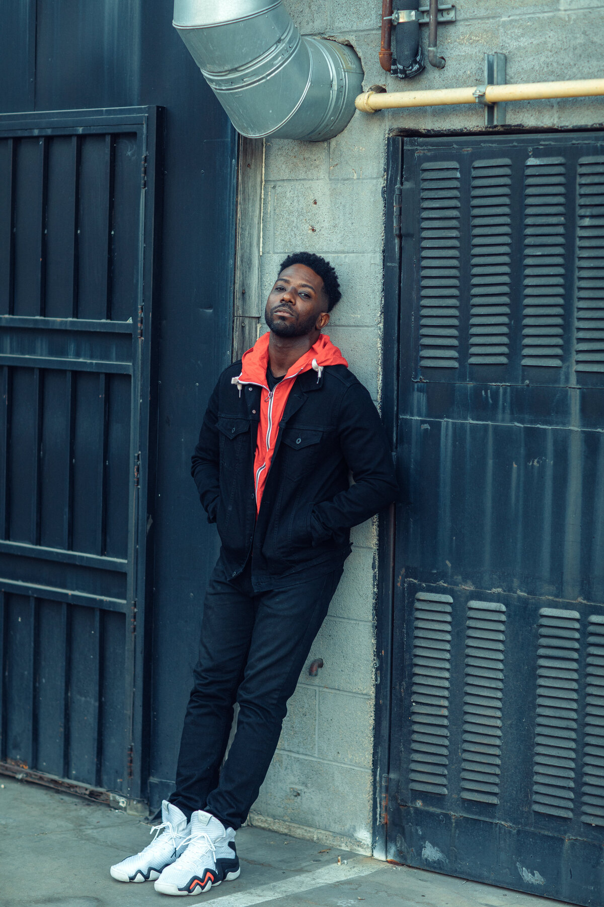 Portrait Photo Of Young Black Man In Orange Hoodie Leaning Against a Wall Los Angeles