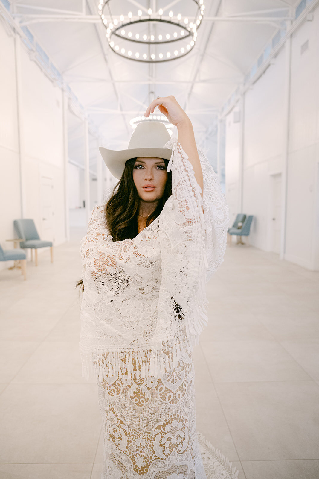 Boho bride lifting hat in airy white hall at The Videre Estate wedding venue in their renovated, Stables Lodge in Austin, Texas.