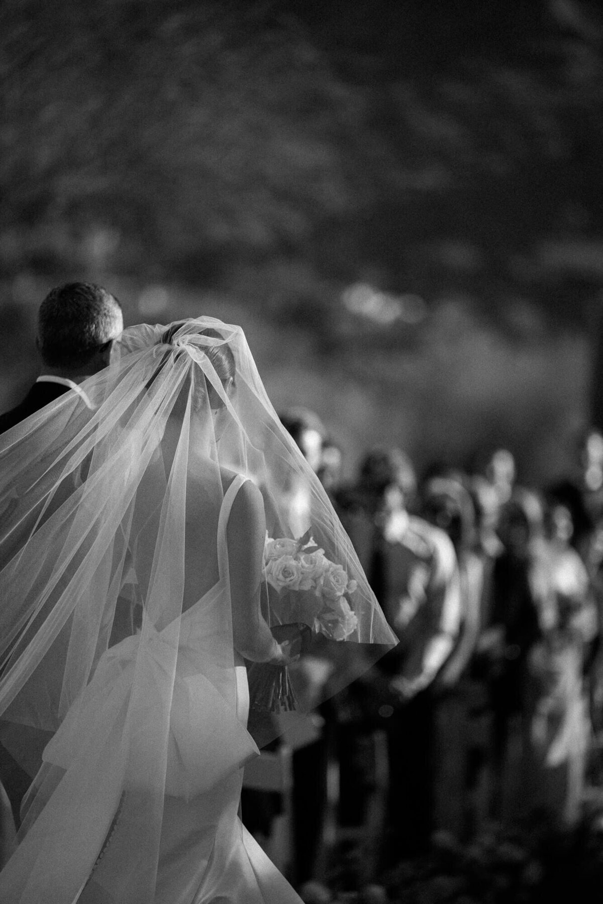 Bride walking down the aisle with her father as sunlight catches her veil, captured by a luxury wedding photographer in Scottsdale.