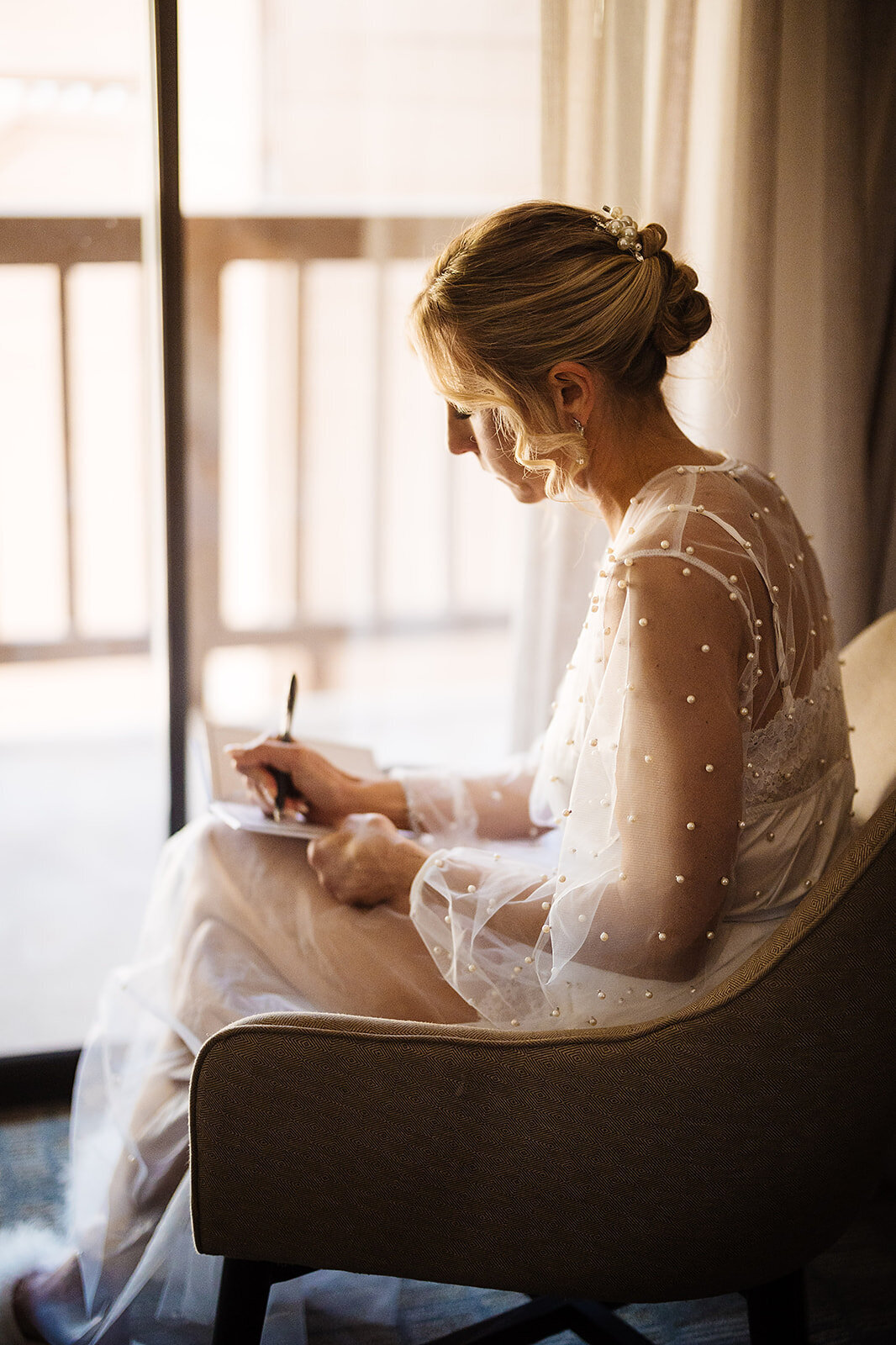 Bride writes a letter to her husband on her wedding morning in a white pearled robe.