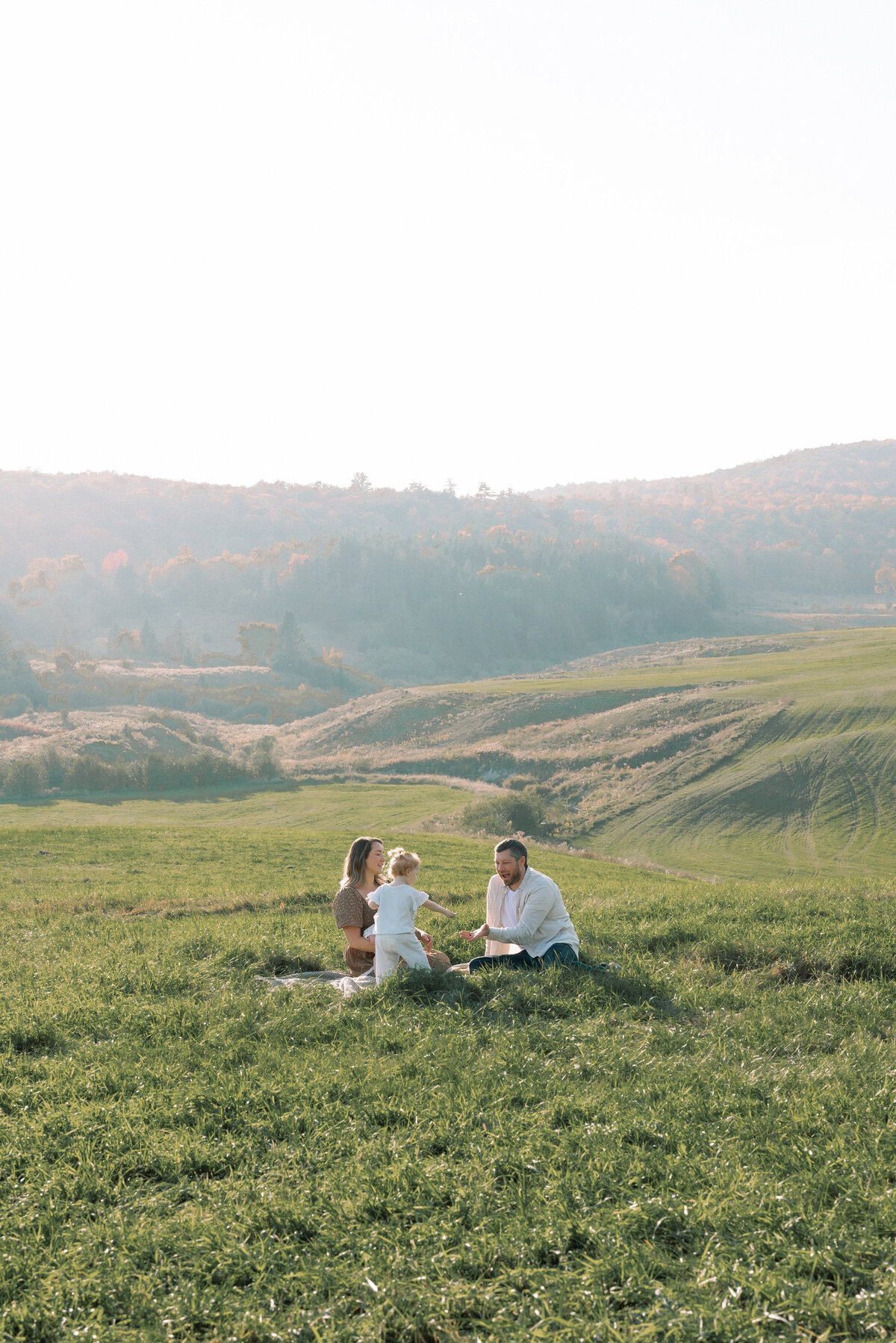 Family sitting down in a field with rolling hills in Ottawa