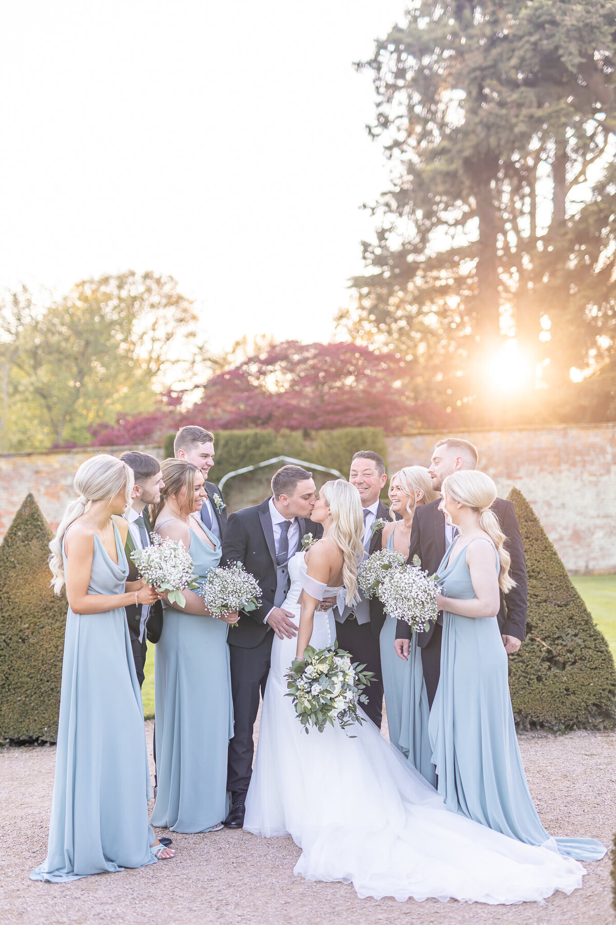 Bride and groom kissing surrounded by the bridal party at Combermere Abbey Cheshire