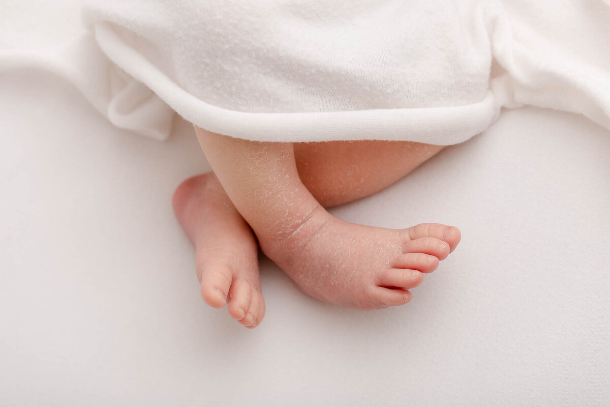 Close-up of baby's feet peeking out under a white blanket. Photo from a Portland Oregon newborn photography session.