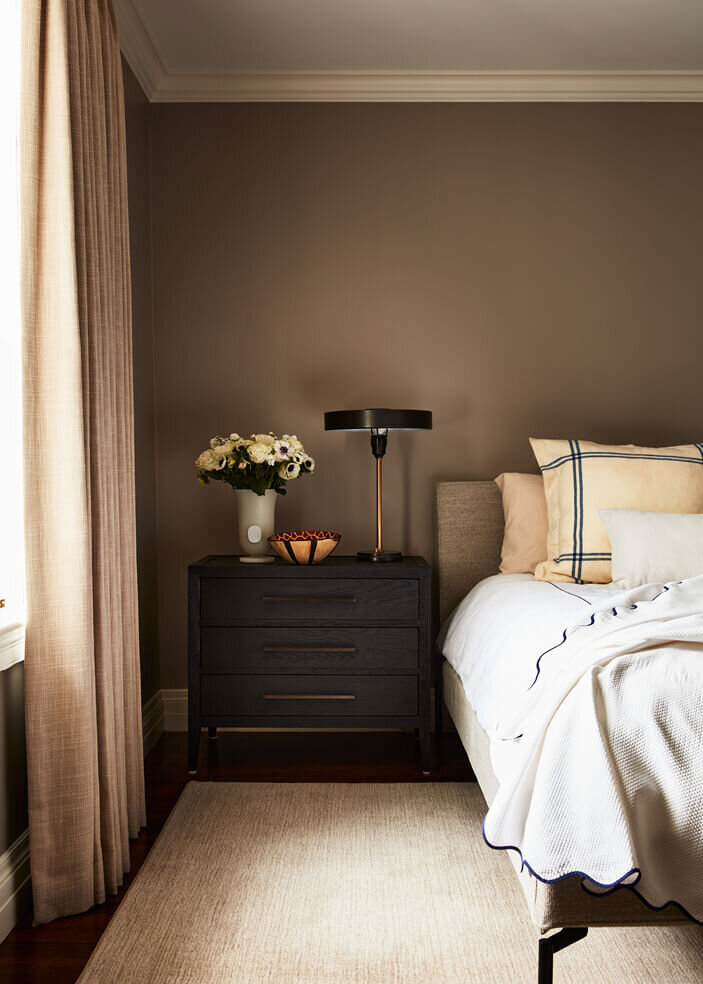 A Boston interior decorator creates a moody bedroom with a modern bed and black bedside tables, balancing dark tones with a refined aesthetic.