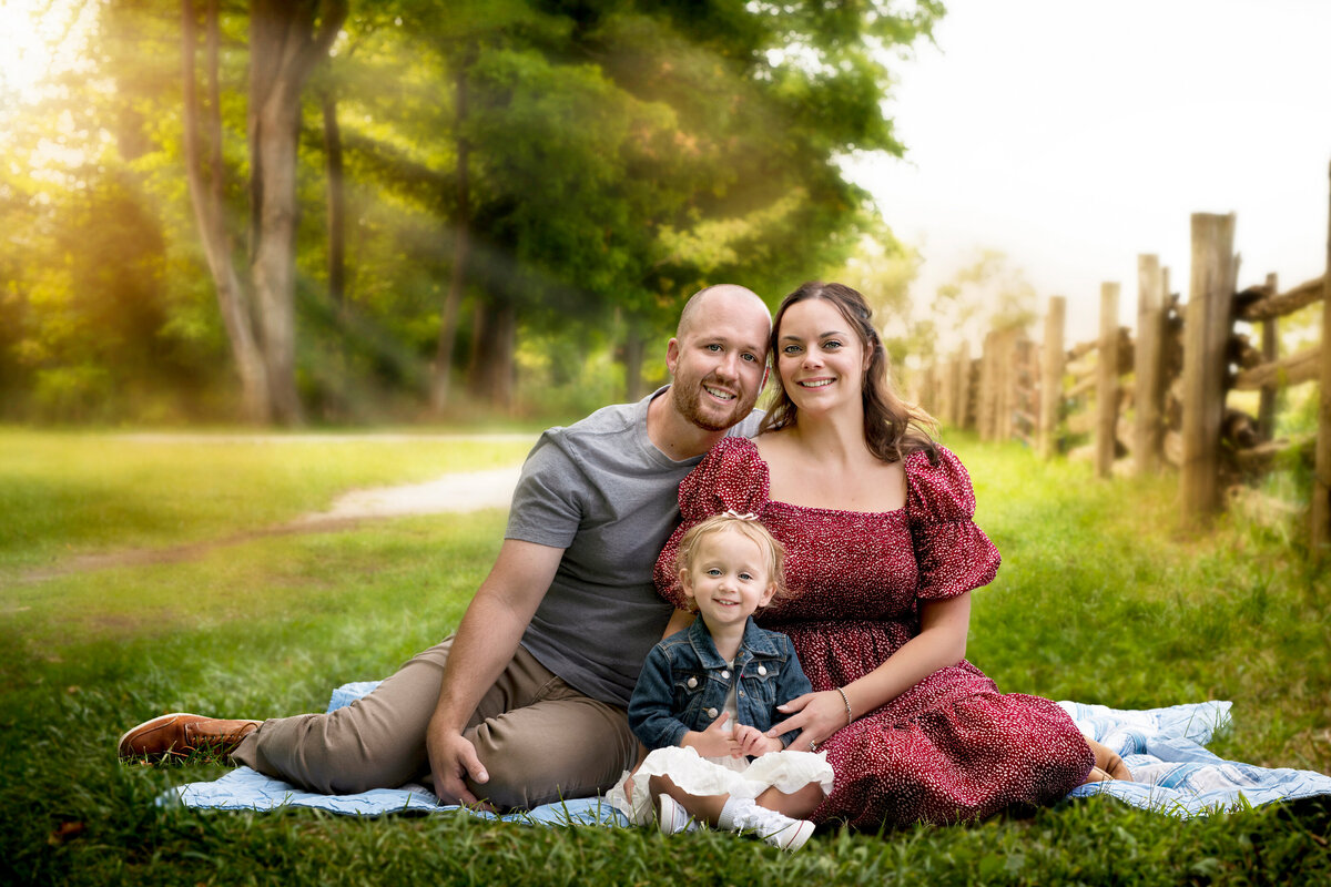 A joyful family sits on a quilt in Bronte Provincial Park in Oakville, Ontario, surrounded by golden summer light and rustic fences.