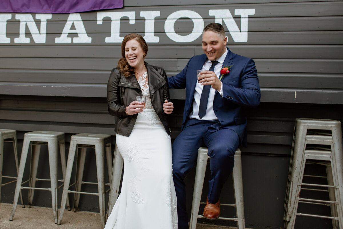 A candid laughing moment of a bride and groom having a drink at an outdoor bar. Captured by Fort Worth wedding photographer, Megan Christine Studio