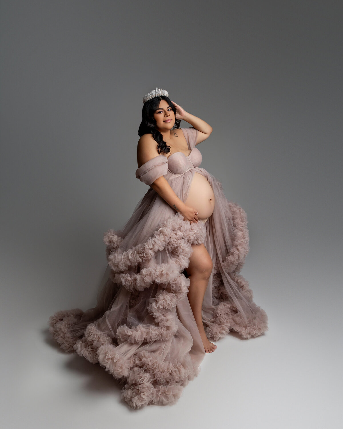 Radiant mother-to-be captured in a soft mauve ruffled gown, lovingly holding her baby bump with a serene smile against a clean, minimalist backdrop. A breathtaking maternity portrait by Inland Empire maternity photographer Kaitlyn Dawn Photography.