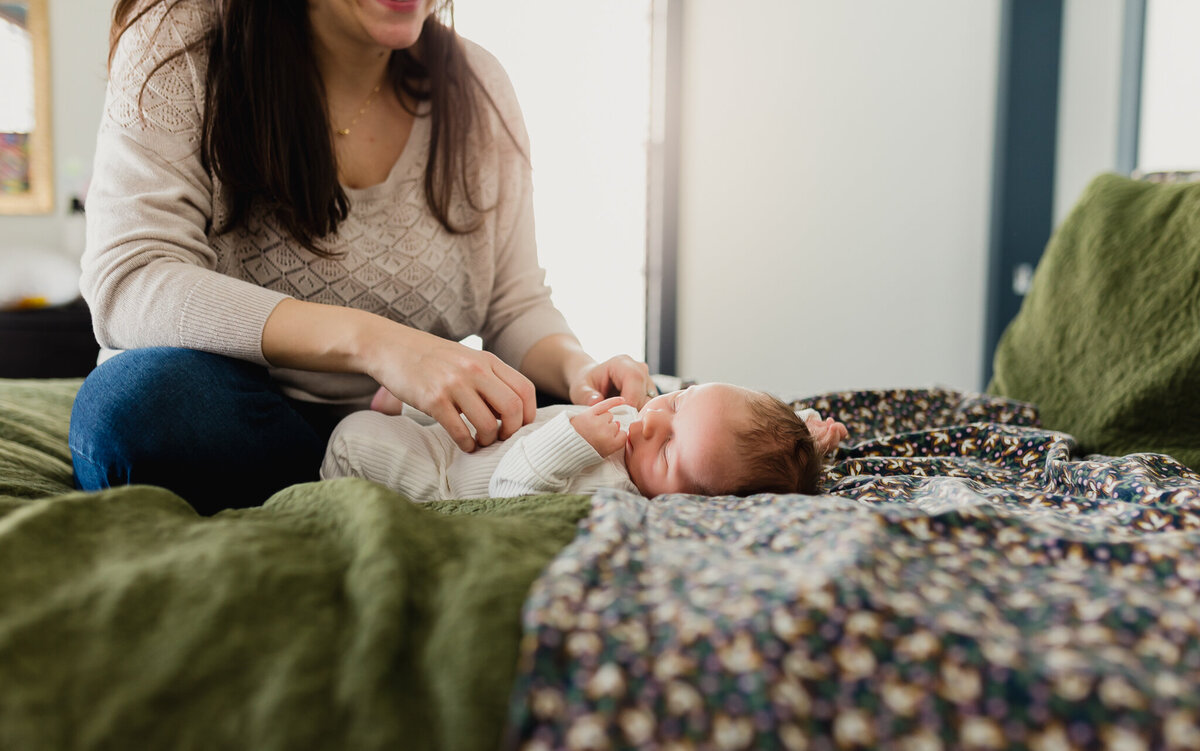 mother snuggles newborn on bed.