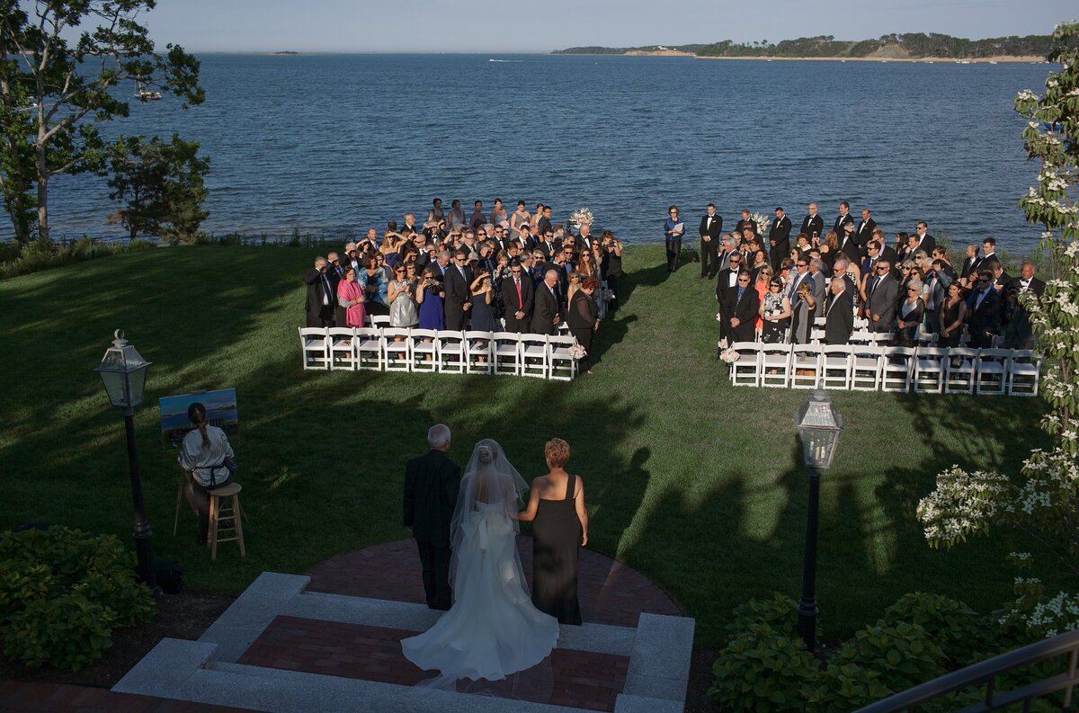 Bride walks towards ceremony overlooking water at Wequassett