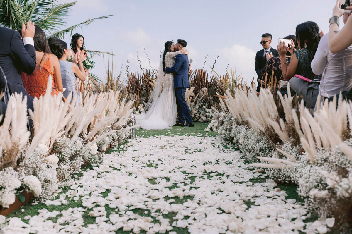 The bride and groom are kissing at the wedding ceremony as the guests cheer them at Bali, Indonesia. Image by Jenny Fu Studio