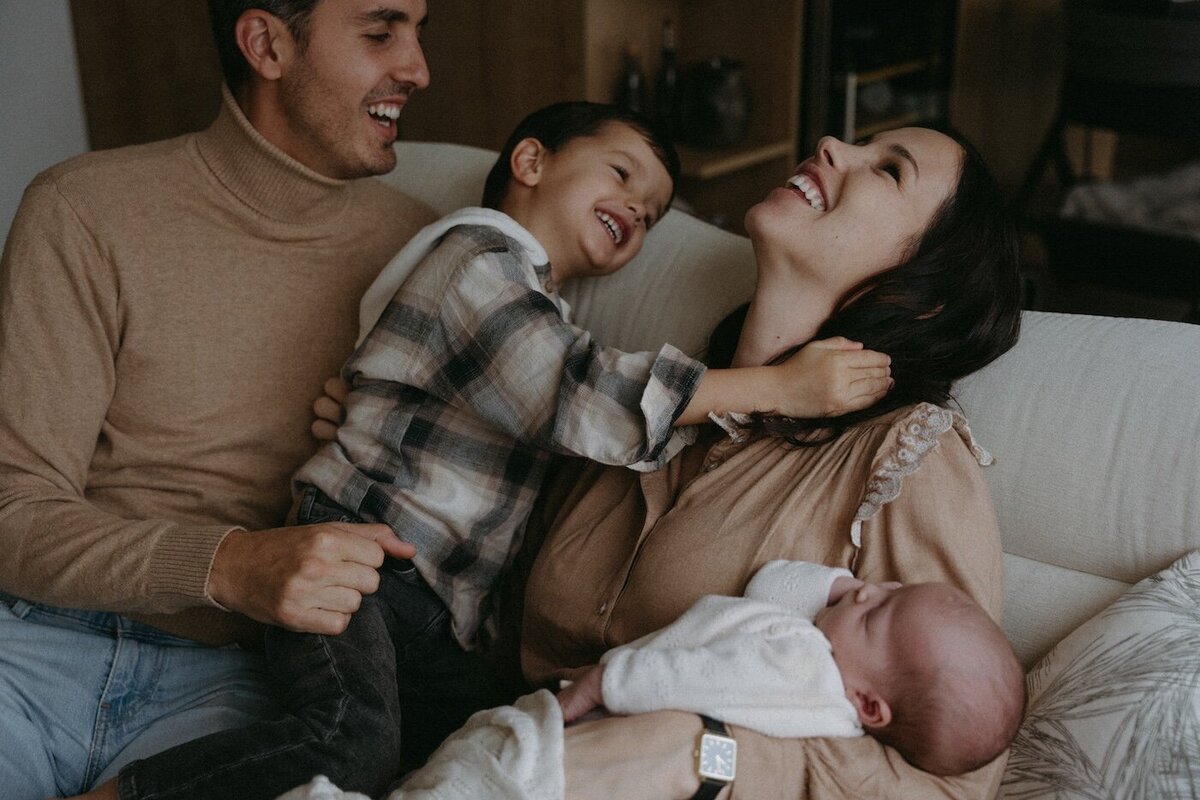 La famille réunie sur le canapé, rires et complicité entre la mère, le père et leur fils, pendant que le bébé dort paisiblement. Photo par Kamescop.