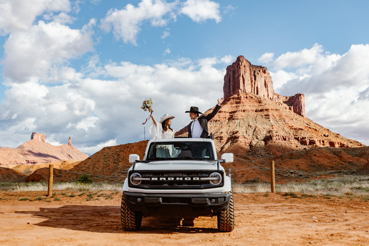 A bride and groom celebrate out of the sunroof of their Ford Bronco on their elopement day in Moab