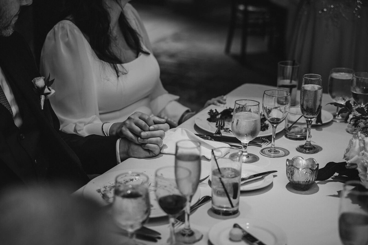 A couple holding hands while they sit at a wedding reception table 