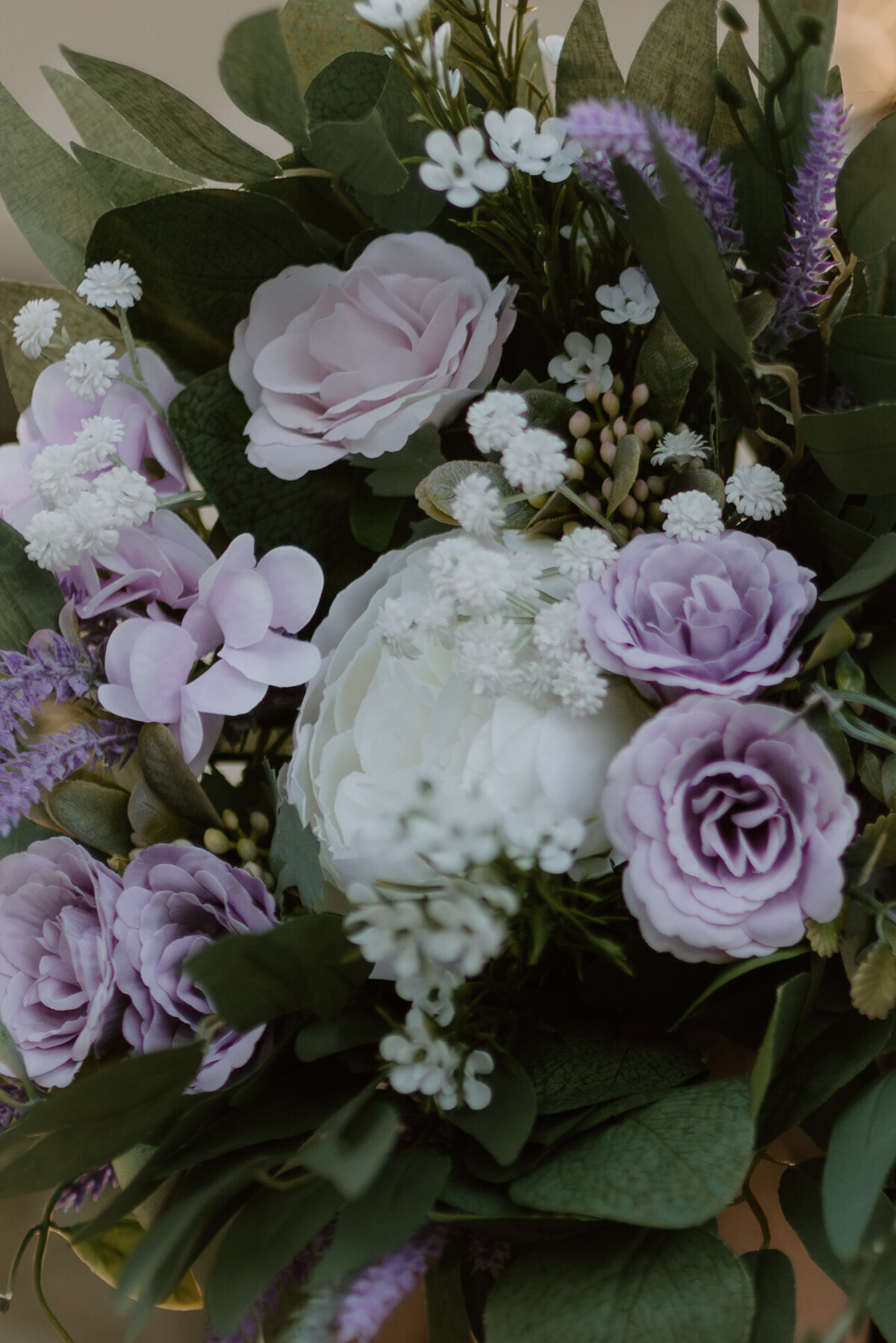 a bridal bouquet that consists of purple and white roses with greenery.