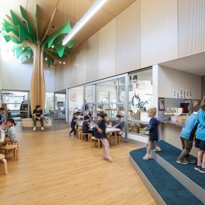 Spacious indoor school area featuring students seated in an open, high-ceiling common space with natural light.
