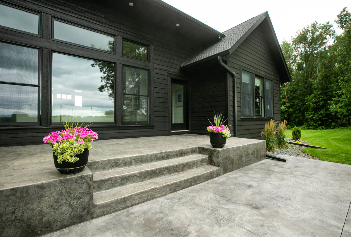Exterior view of custom home in Otsego, Minnesota with black siding, large patio and windows built by Cornerstone Custom Builds