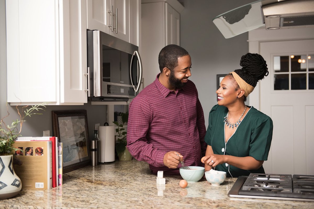 Couple standing together in kitchen with granite countertops smiling at one another as they gather ingredients for cookies