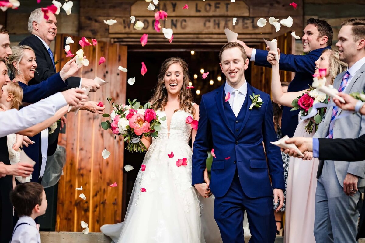 A colorful wedding exit with the bride and groom walking through a shower of rose petals, guests cheering and celebrating the moment.