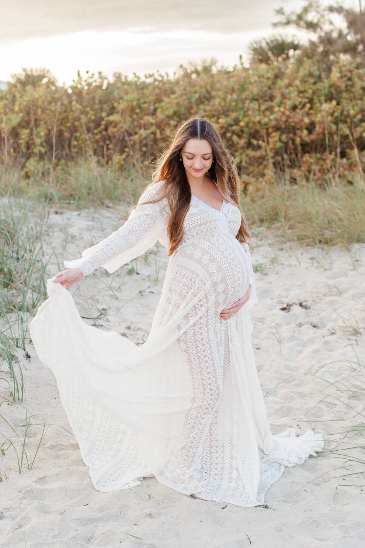 Stunning pregnant mom in a white lace gown swinging it in the wind while looking down at her belly
