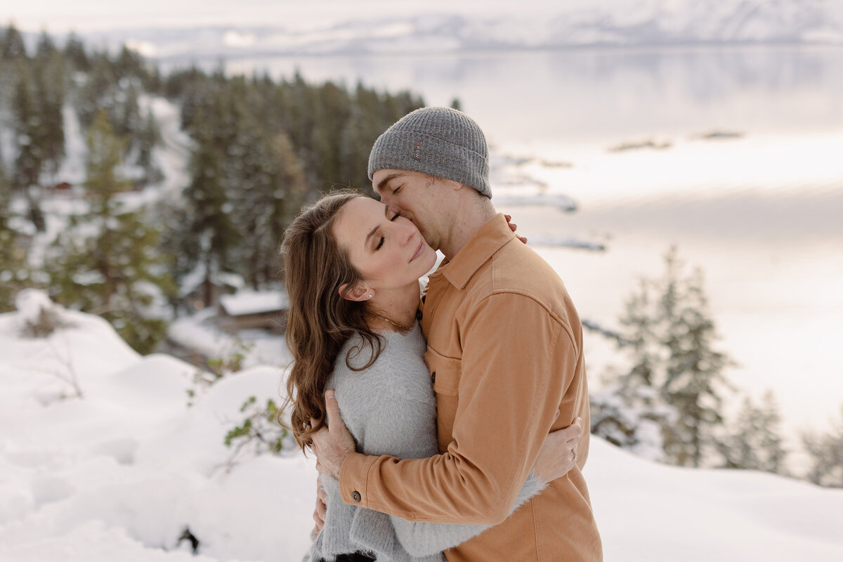 man kissing a womans neck while holding her in a snowy field