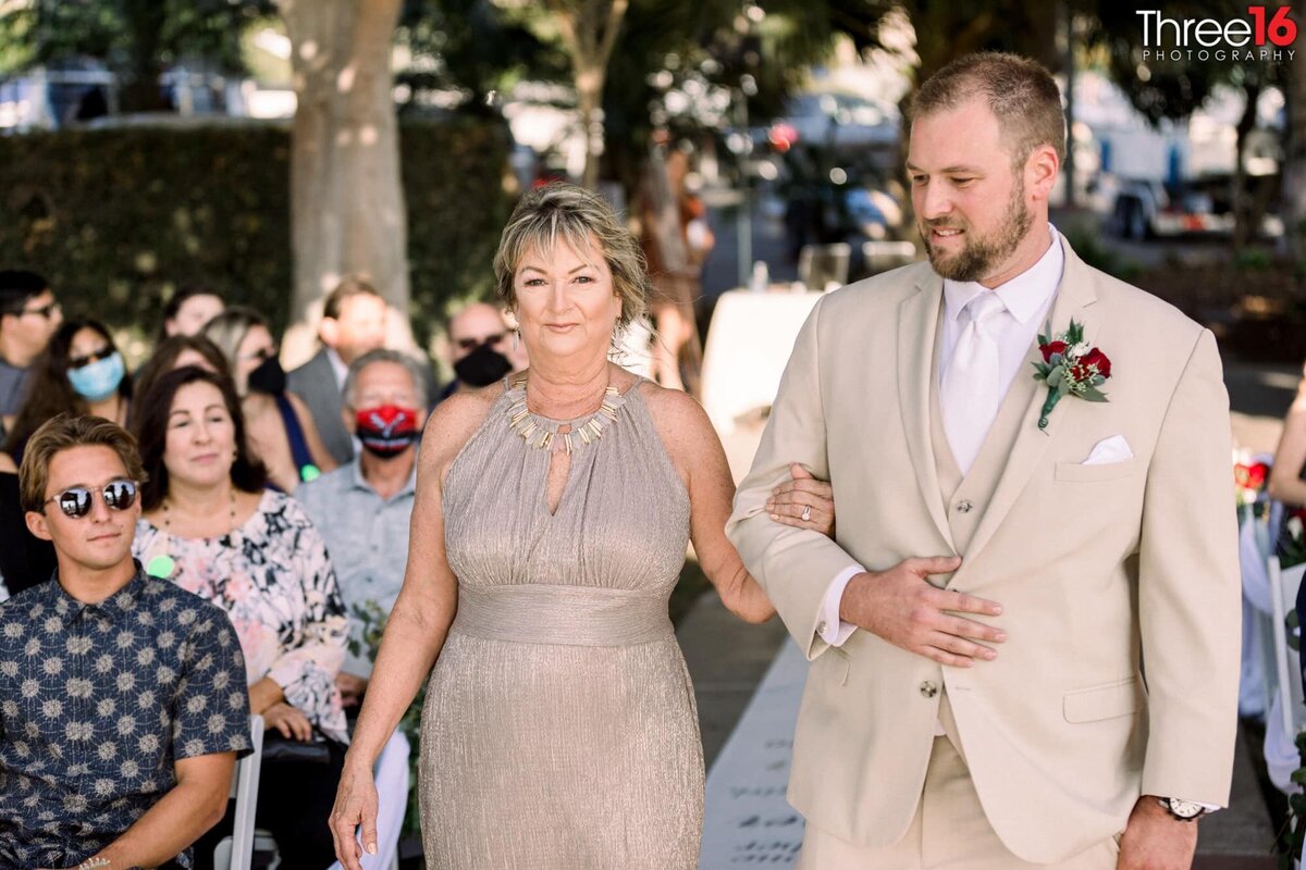 Groom escorts his mother down the aisle to her seat
