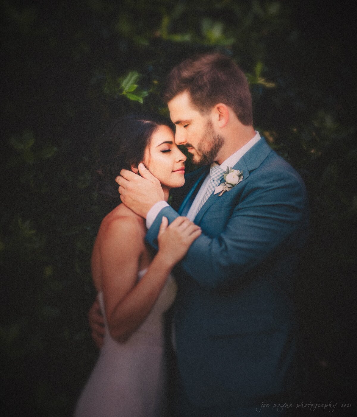A wedding couple holding each other close with their faces touching.