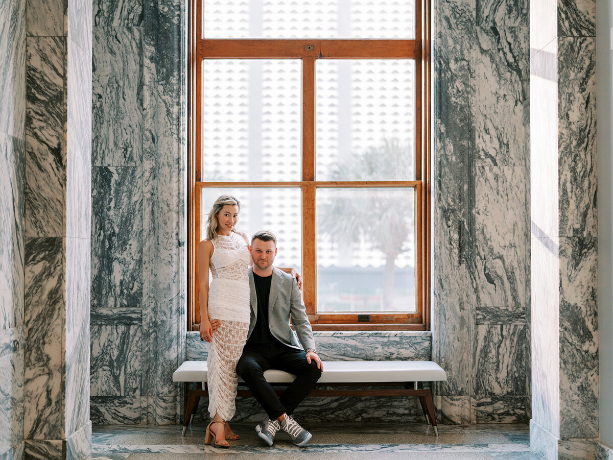 Couple posing near a wooden-framed window with marble walls inside Le Meridien hotel.