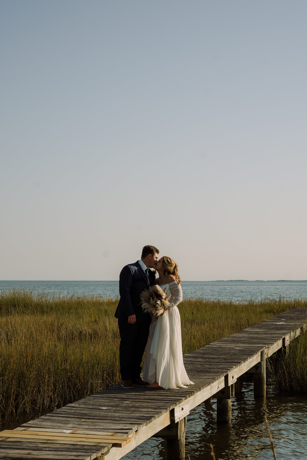 bride and groom kissing on long deck over water at destination wedding