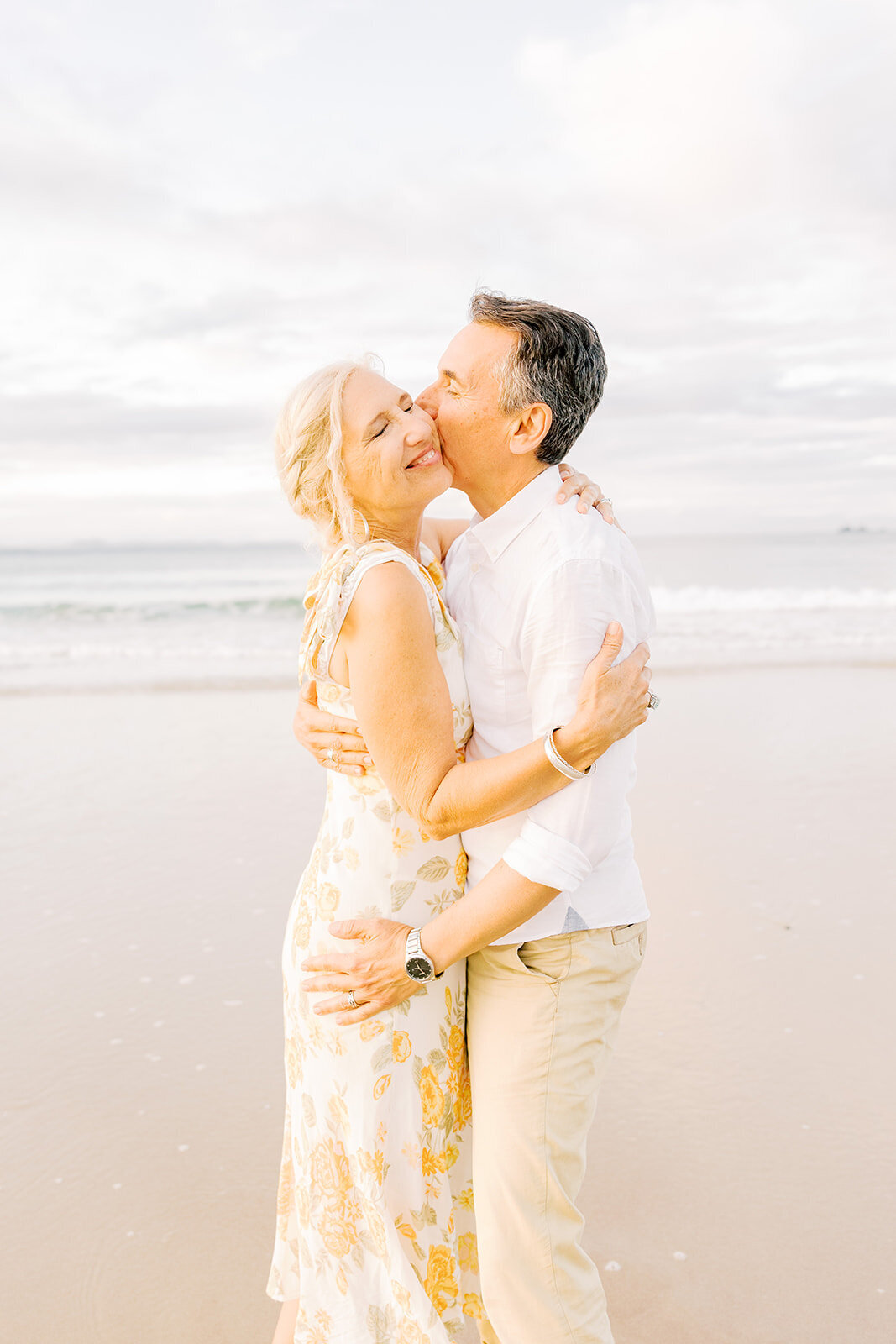 husband kissing wife on the cheek on beach