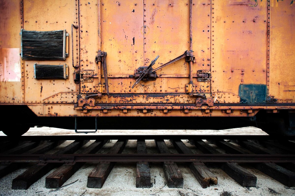 The side of an old rusted orange and yellow train car