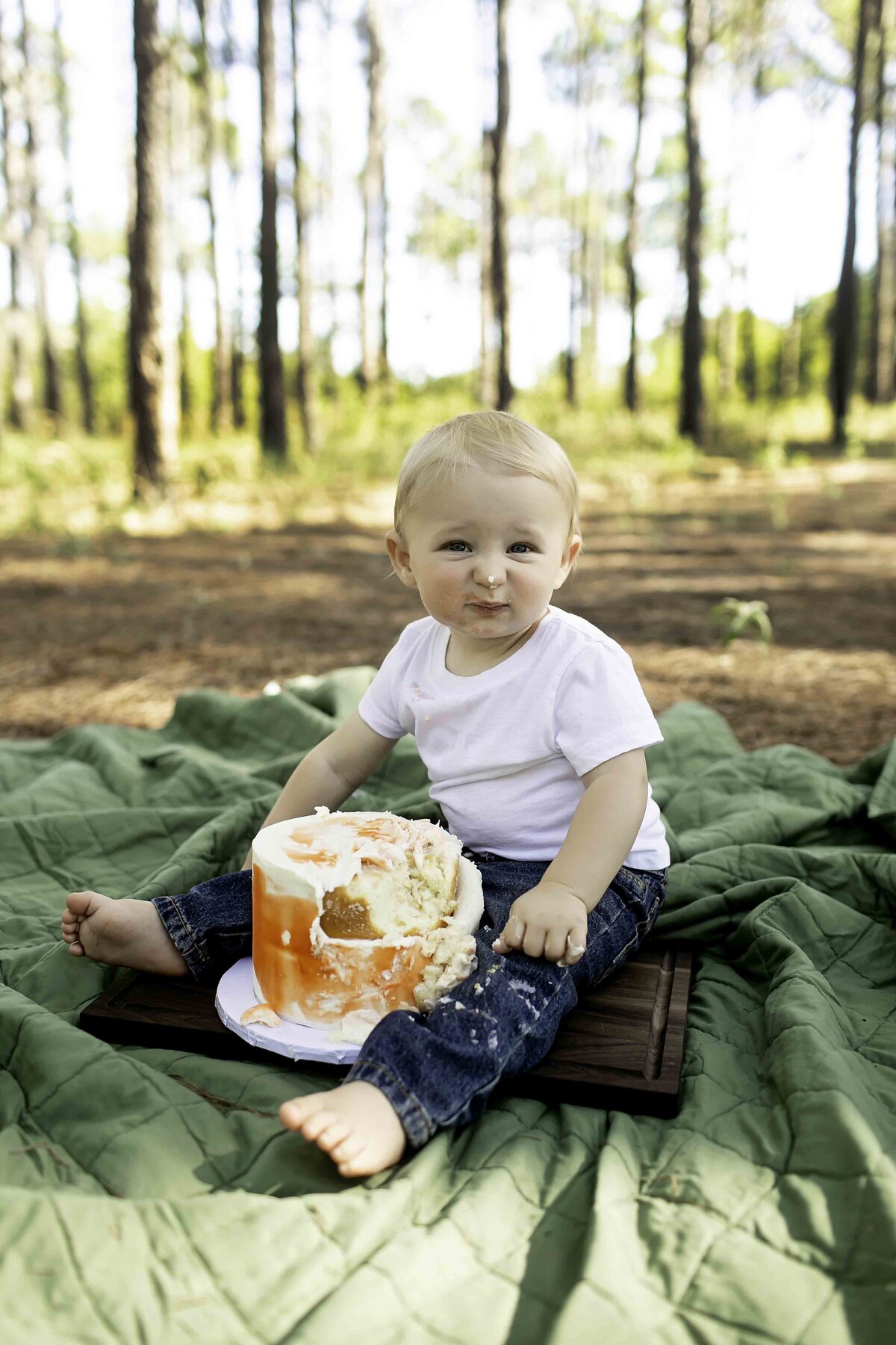 Birthday boy wearing overalls and suspenders, joyfully smashing his birthday cake with frosting on his hands, surrounded by pine trees