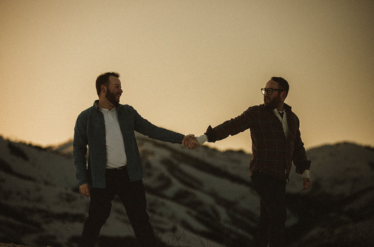 two men hold hands with mountains of utah behind them 